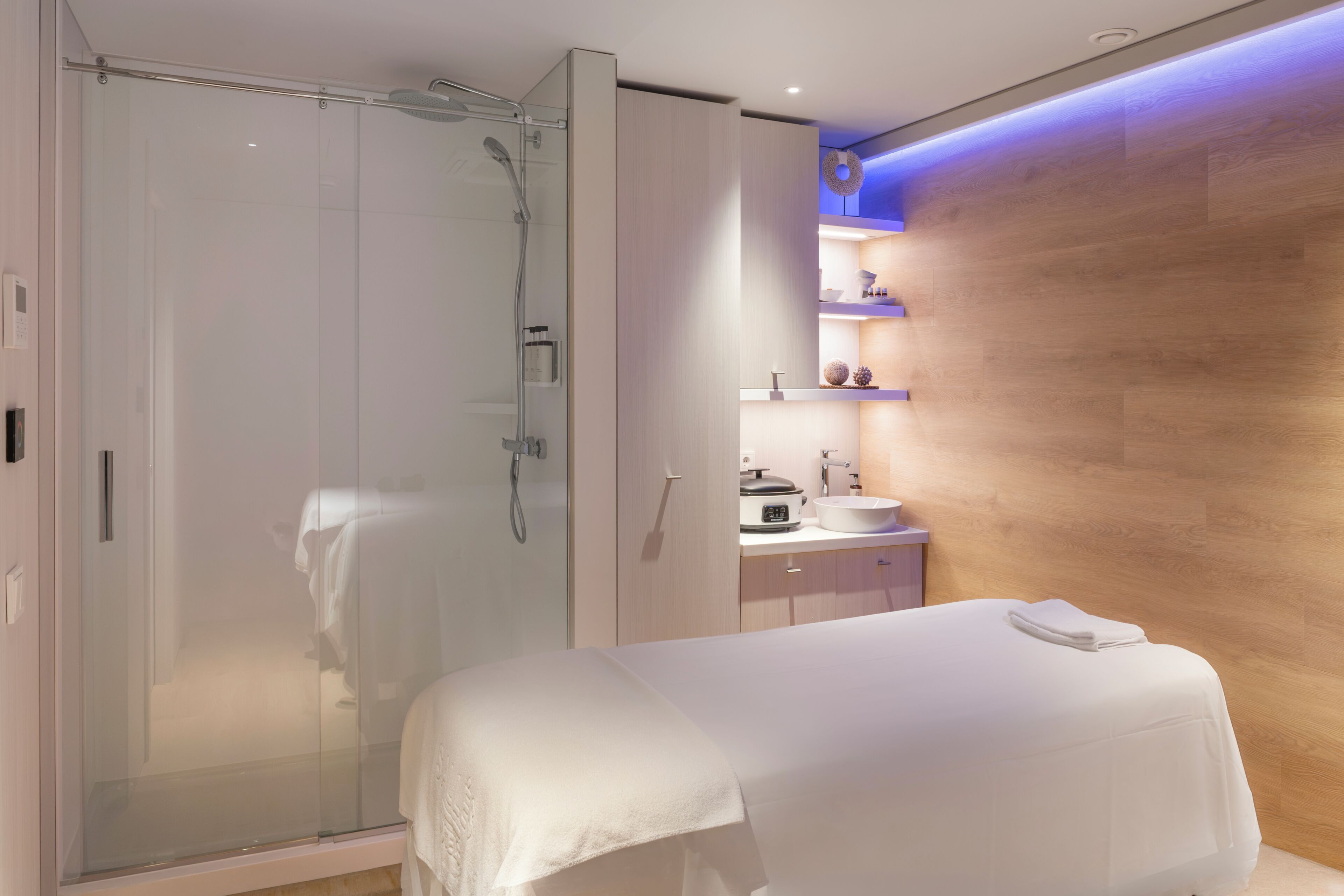 Un baño moderno con ducha de vidrio, tocador de madera con lavamanos y una camilla de masaje.