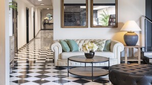 A hotel lobby with a checkered floor, a white sofa with green cushions, a round coffee table, and two wall-mounted mirrors. - Salles Hotel Aeroport de Girona (Riudellots de la Selva)