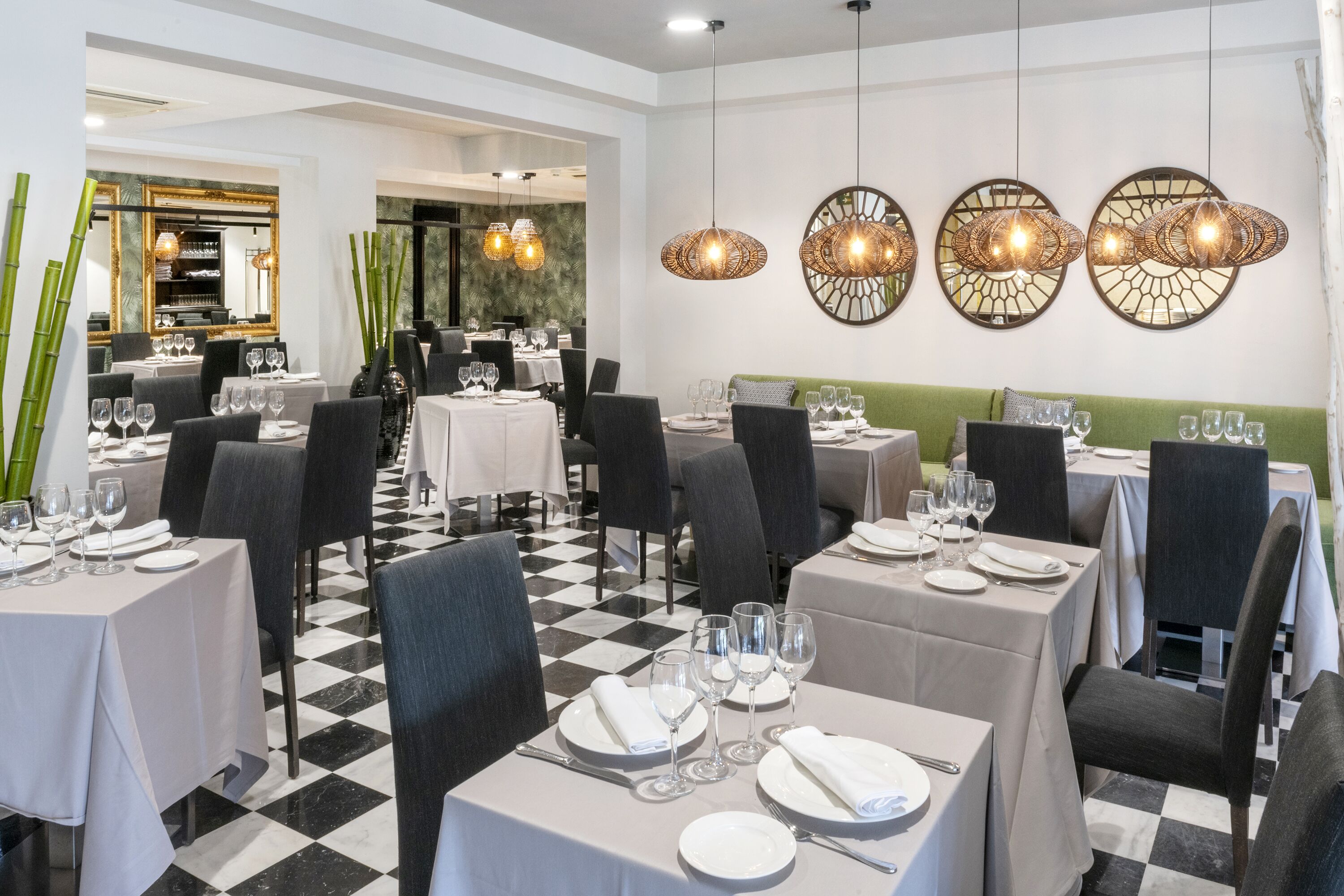 Un restaurante con suelo de tablones, mesas redondas con manteles blancos y sillas negras.