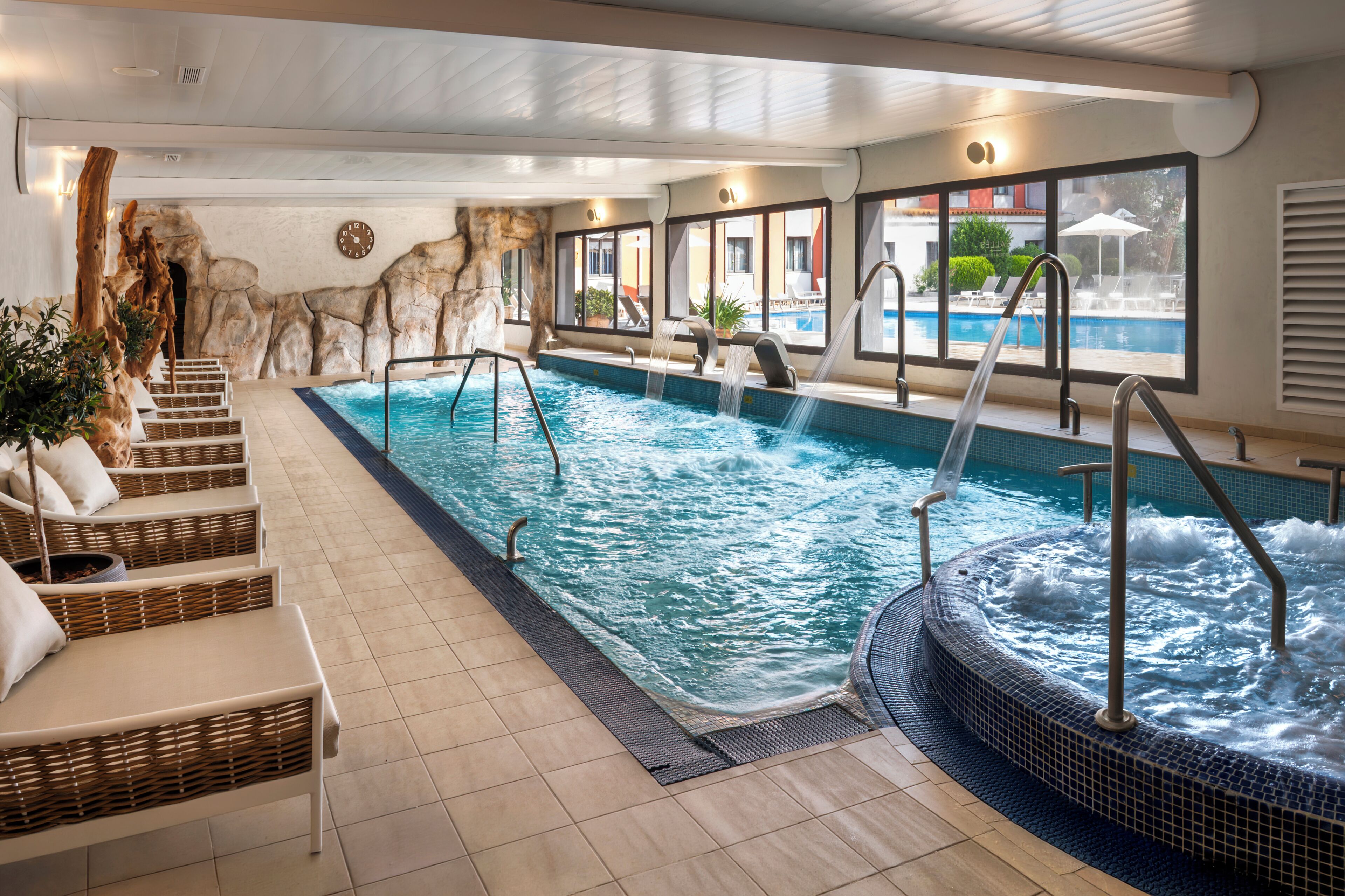 Ein Hotel-Hallenbad mit Whirlpool, Liegestühlen und Blick ins Freie.