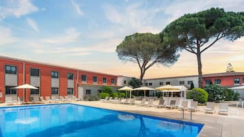 A swimming pool with lounge chairs and umbrellas, surrounded by a building with a tiled roof.