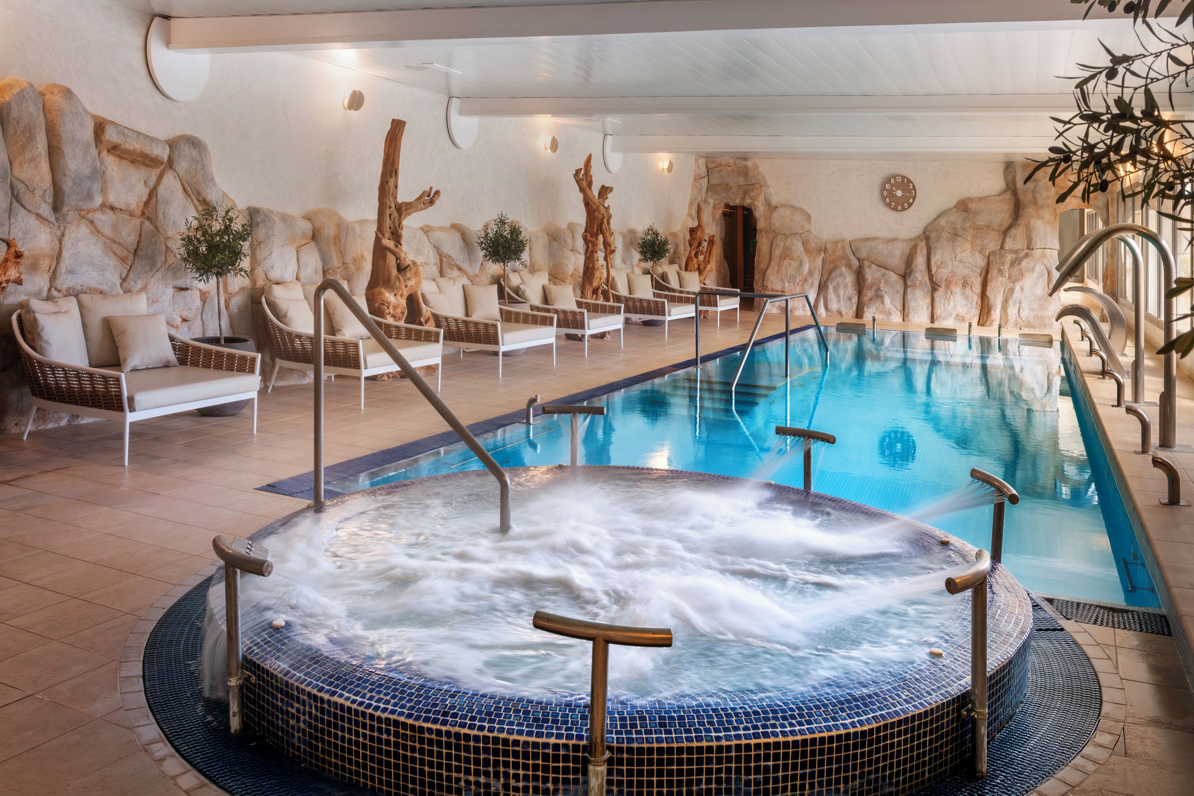 A swimming pool with a hot tub, lounge chairs, and a stone wall backdrop.