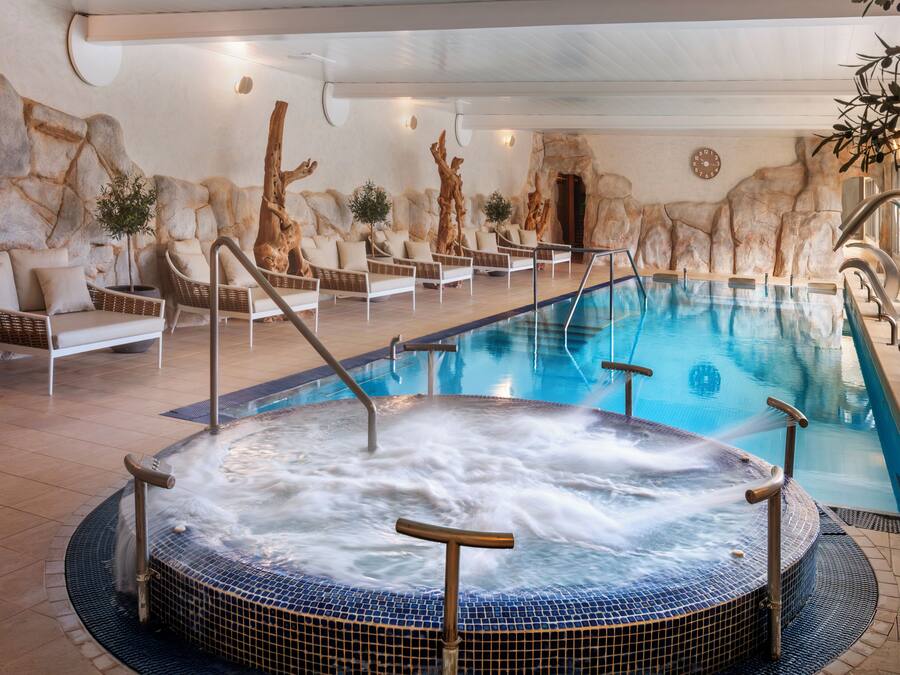Une piscine avec un jacuzzi, des chaises longues et un mur en pierre en arrière-plan.