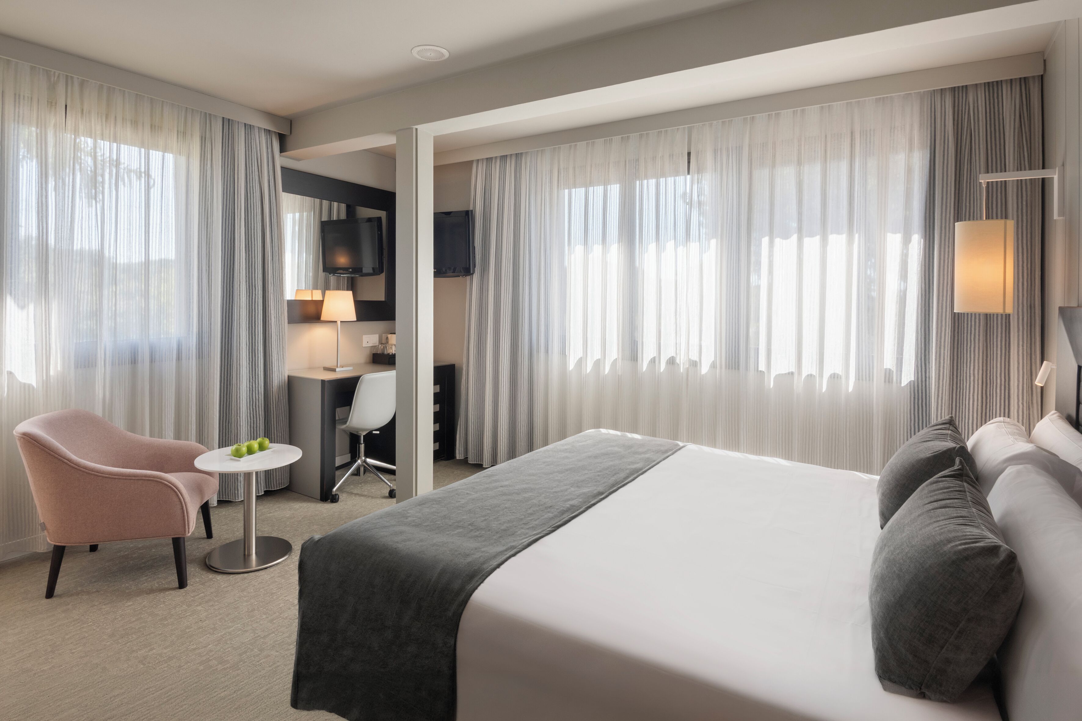 A hotel room with a bed, a desk, a chair, and a TV.
