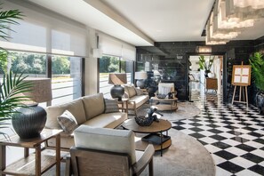 A modern hotel lobby with a checkered floor, a sofa set, a dining area, and a view of the outdoors. - Salles Hotel Aeroport de Girona (Riudellots de la Selva)