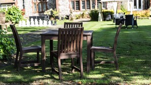 A dining area with a table and chairs, a stone building in the background, and a well-maintained lawn. - Dales Country House (Sheringham)
