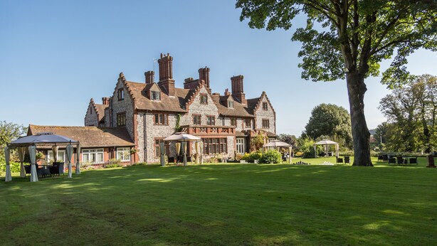 A large stone building with multiple chimneys, a lawn, and outdoor seating areas. - Dales Country House (Sheringham)
