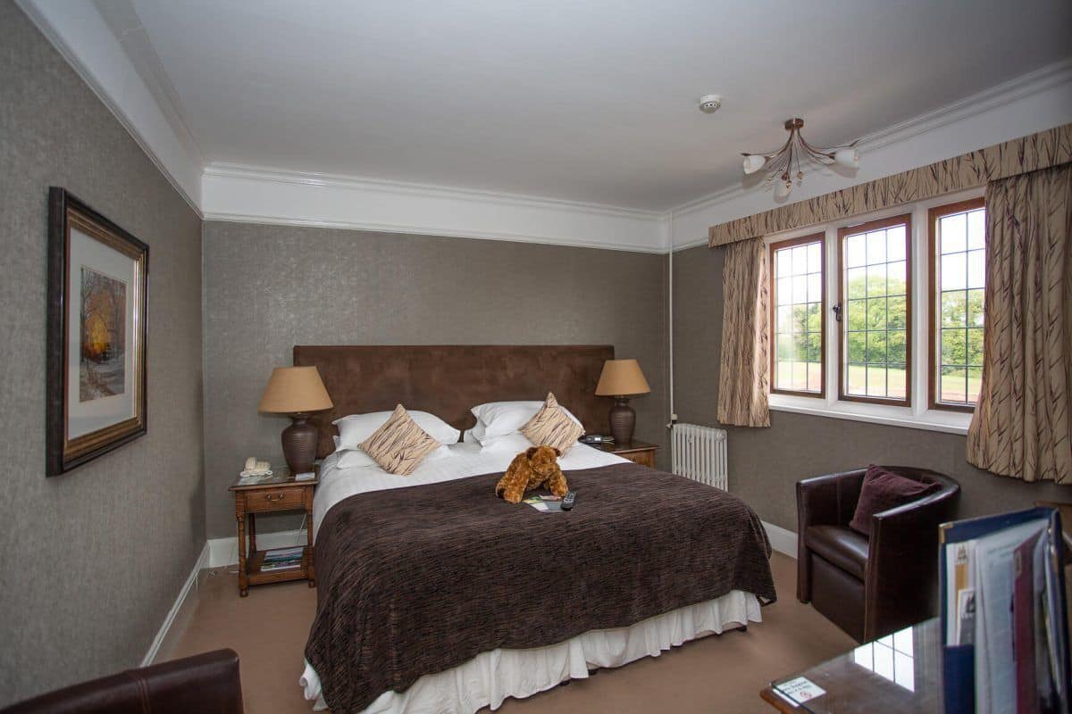 A neatly arranged bedroom with a large bed, two bedside tables, a chair, and a window with curtains.