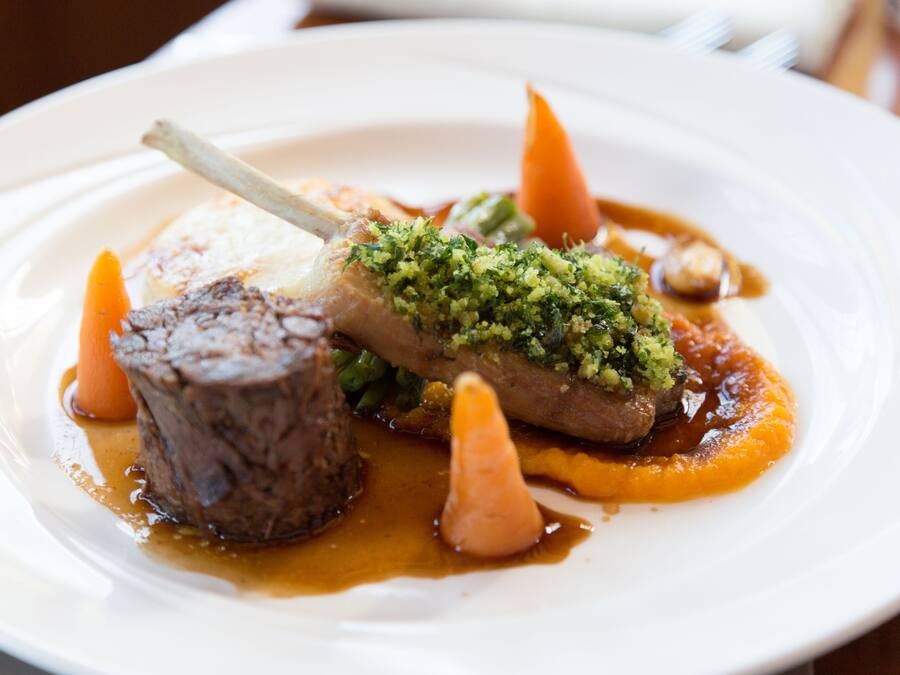 Une assiette de nourriture comprenant un jarret d’agneau, des carottes et une garniture de légumes verts.