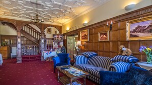 A grand lobby with a red carpet, a staircase, a blue sofa, and a chandelier. - Dales Country House (Sheringham)