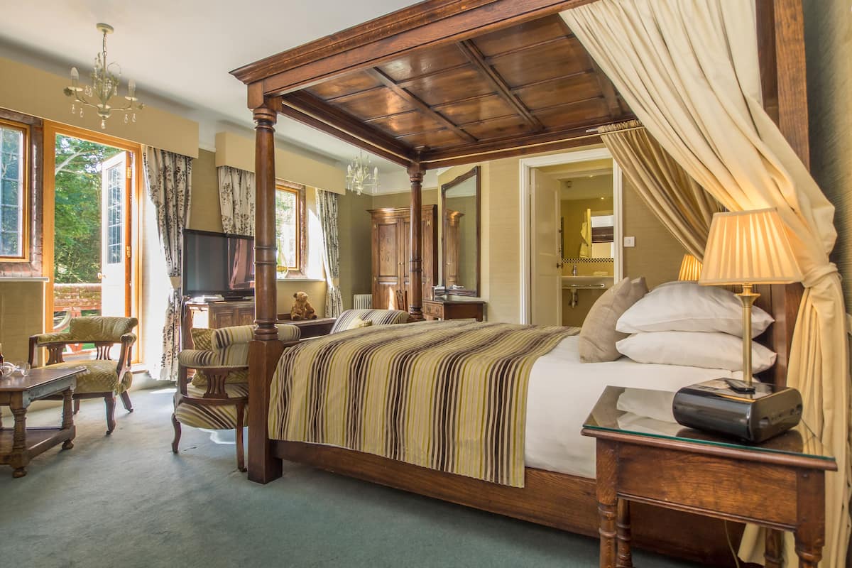 A four-poster bed with a striped bedspread, wooden furniture, and a chandelier.
