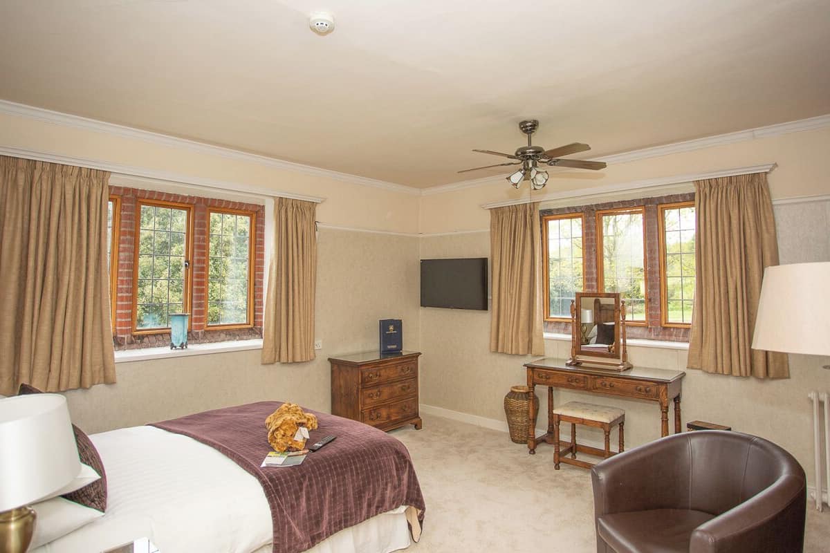 A bedroom with a bed, a desk, a chair, a ceiling fan, and a window with curtains.