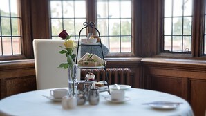 A round table with a white tablecloth, a tiered stand with sandwiches, a vase with a single rose, and tea service. - Dales Country House (Sheringham)