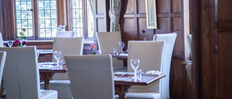 Un comedor con paredes de paneles de madera, sillas blancas tapizadas y una mesa puesta con copas de vino y cubiertos.
