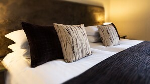 A neatly made bed with white and dark pillows, a dark headboard, and a bedside table with a lamp. - Dales Country House (Sheringham)