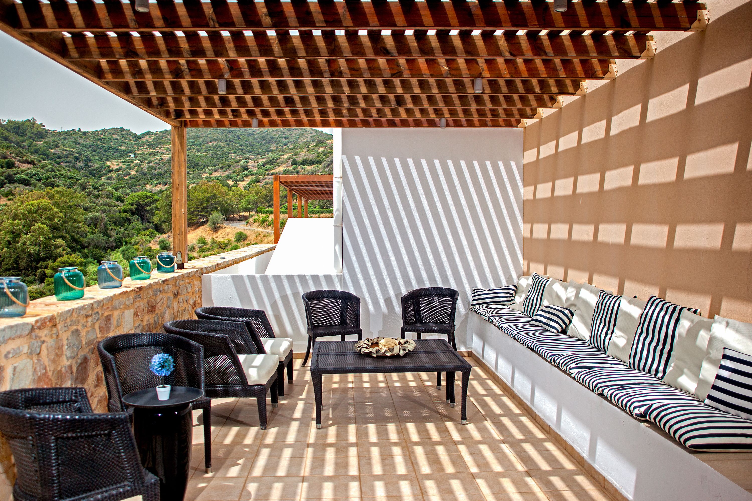 An outdoor patio with wicker furniture, a white sofa, and a view of a hilly landscape.