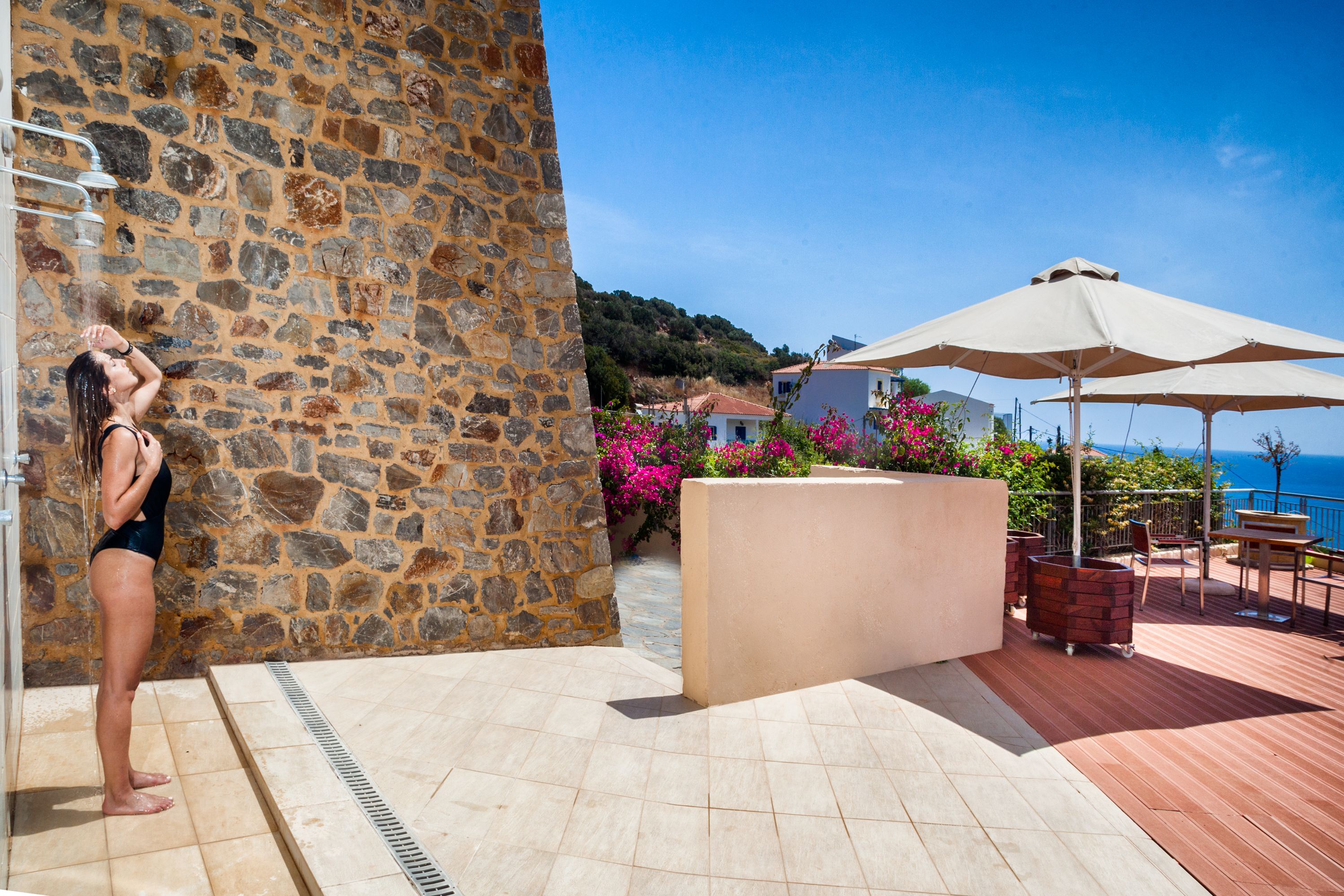 Un muro de piedra, suelo de baldosas, zona de piscina, mobiliario exterior y vista al mar.