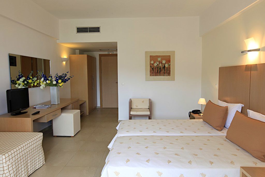 A hotel room with two beds, a desk with a TV, a chair, a bedside table with a lamp, and a painting on the wall.