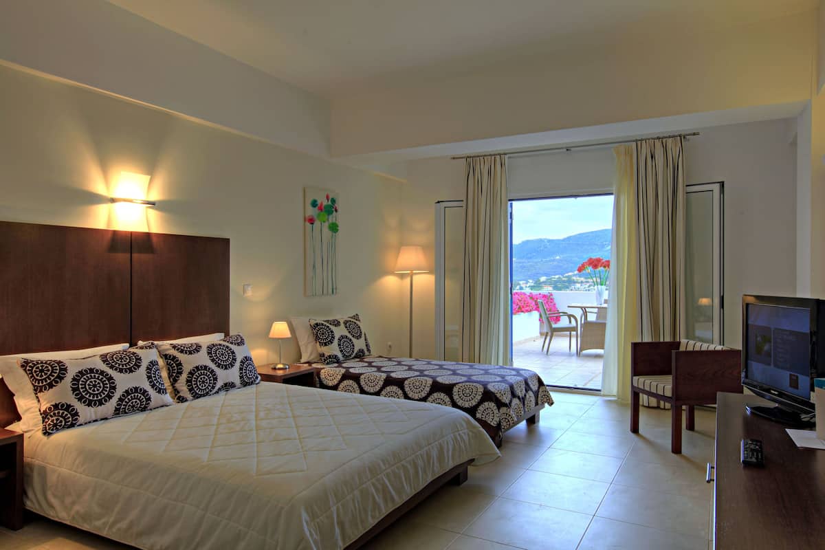 Habitación de hotel con dos camas, televisión, escritorio y balcón con vistas.