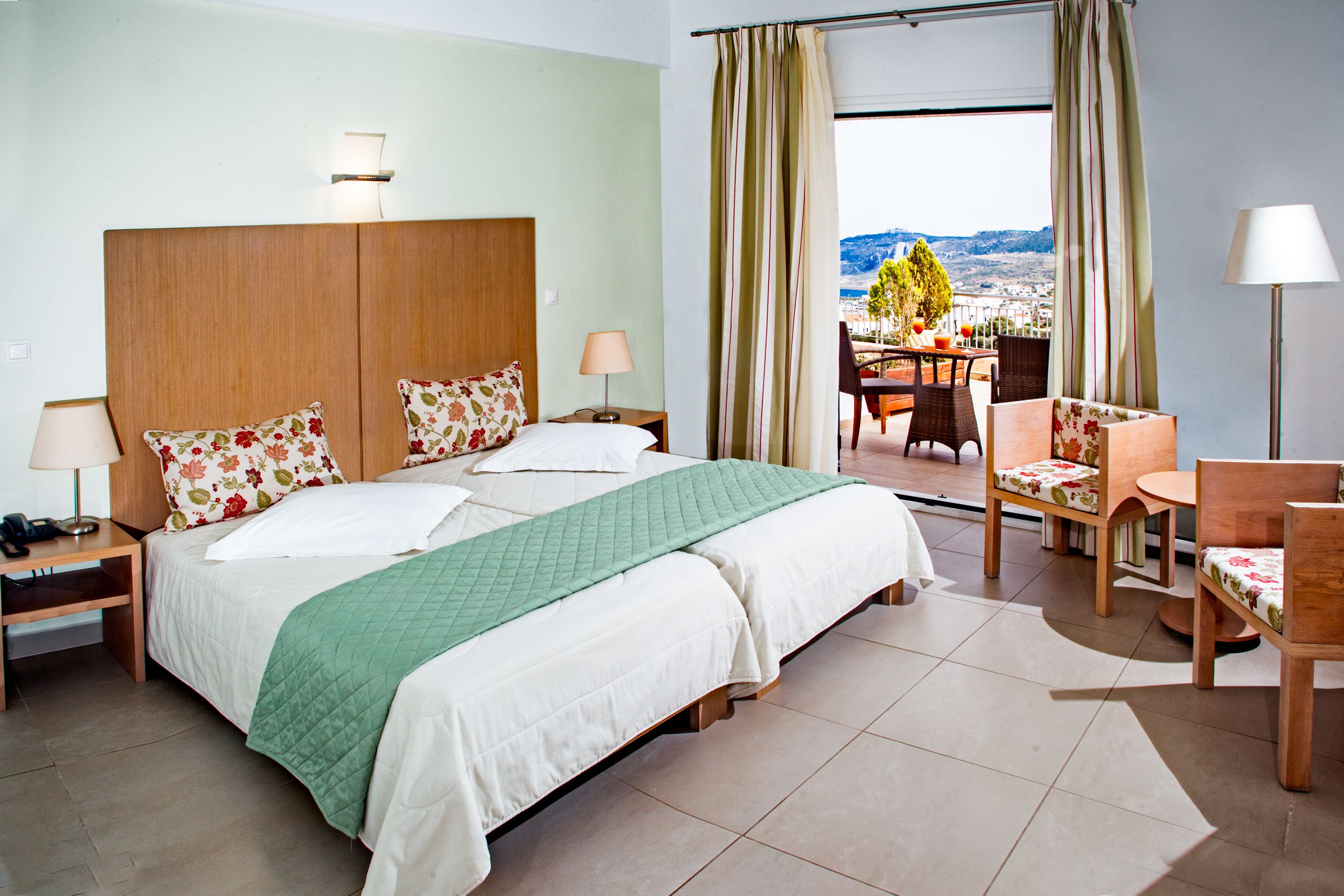 A hotel room with a large bed, two bedside tables, a desk with a chair, and a view of the outdoors.