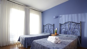 Una habitación de hotel con dos camas, una ventana con cortinas blancas y una pared azul.