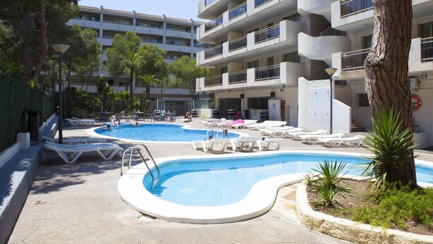 Zona de piscina con sillas de descanso y un edificio al fondo.