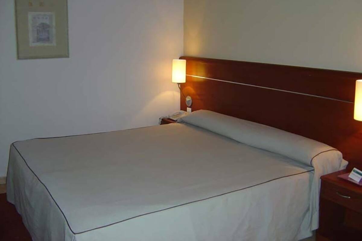 A hotel room with a single bed, a nightstand, and two wall-mounted lamps.