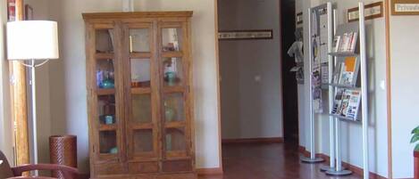 A reception area with a wooden cabinet, a floor lamp, a chair, and a bookshelf with magazines.
