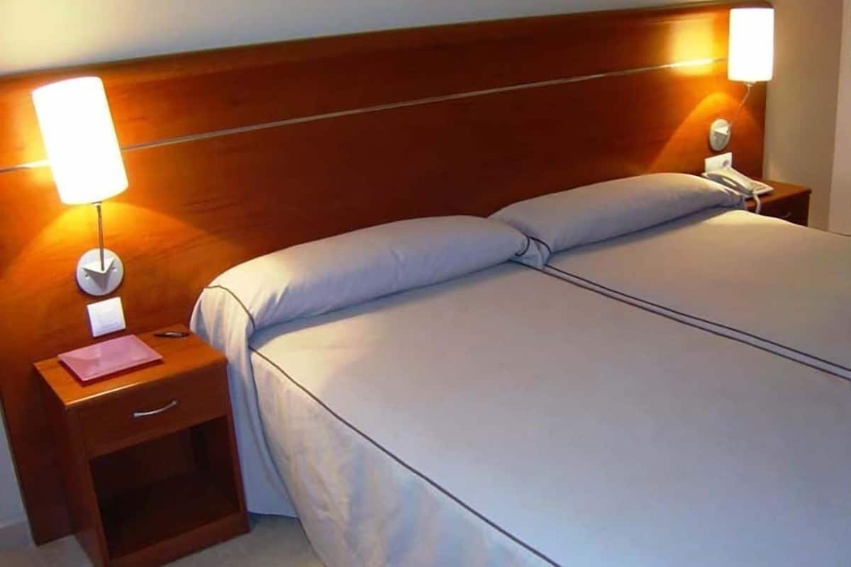 A neatly made bed with a wooden headboard, two bedside tables with lamps, and a small drawer.