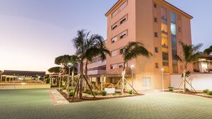 A multi-story hotel with a flat roof, palm trees, and a paved courtyard. - Pato Rojo (Punta Umbría)