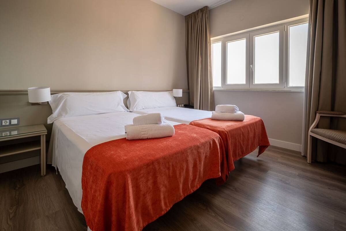 A hotel room with a large bed, two bedside tables, a window with curtains, and a chair.