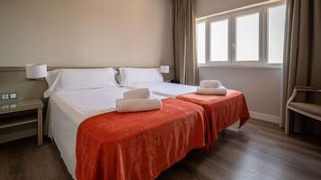 Una habitación de hotel con una cama grande, dos mesitas de noche, una ventana con cortinas y una silla.
