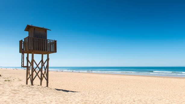 A wooden lifeguard tower on a sandy beach with the ocean in the background. - Pato Rojo (Punta Umbría)