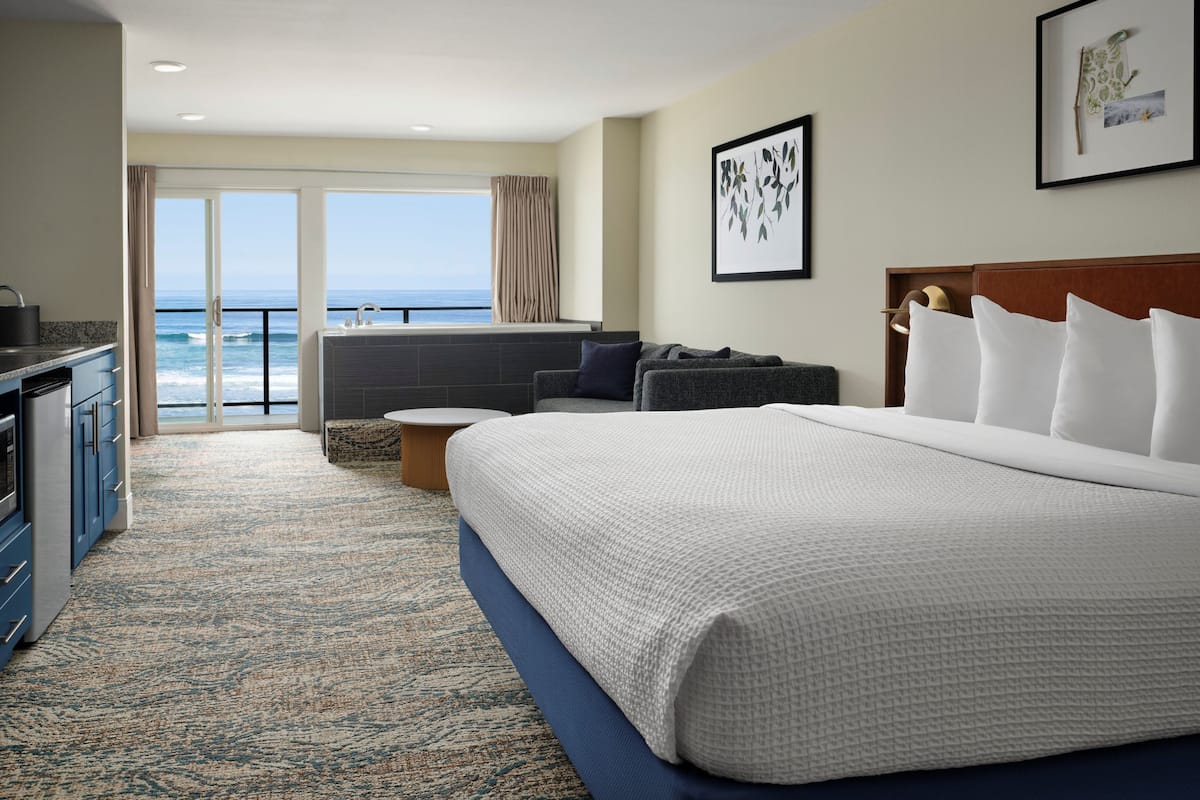 Ein Hotelzimmer mit einem großen Bett, einer Sitzecke mit Meerblick, einer Küchenzeile und einem Balkon.