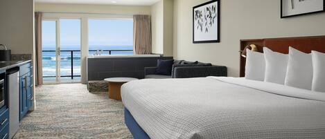 Une chambre d’hôtel dotée d’un grand lit, d’un coin salon avec vue sur l’océan, d’une kitchenette et d’un balcon.