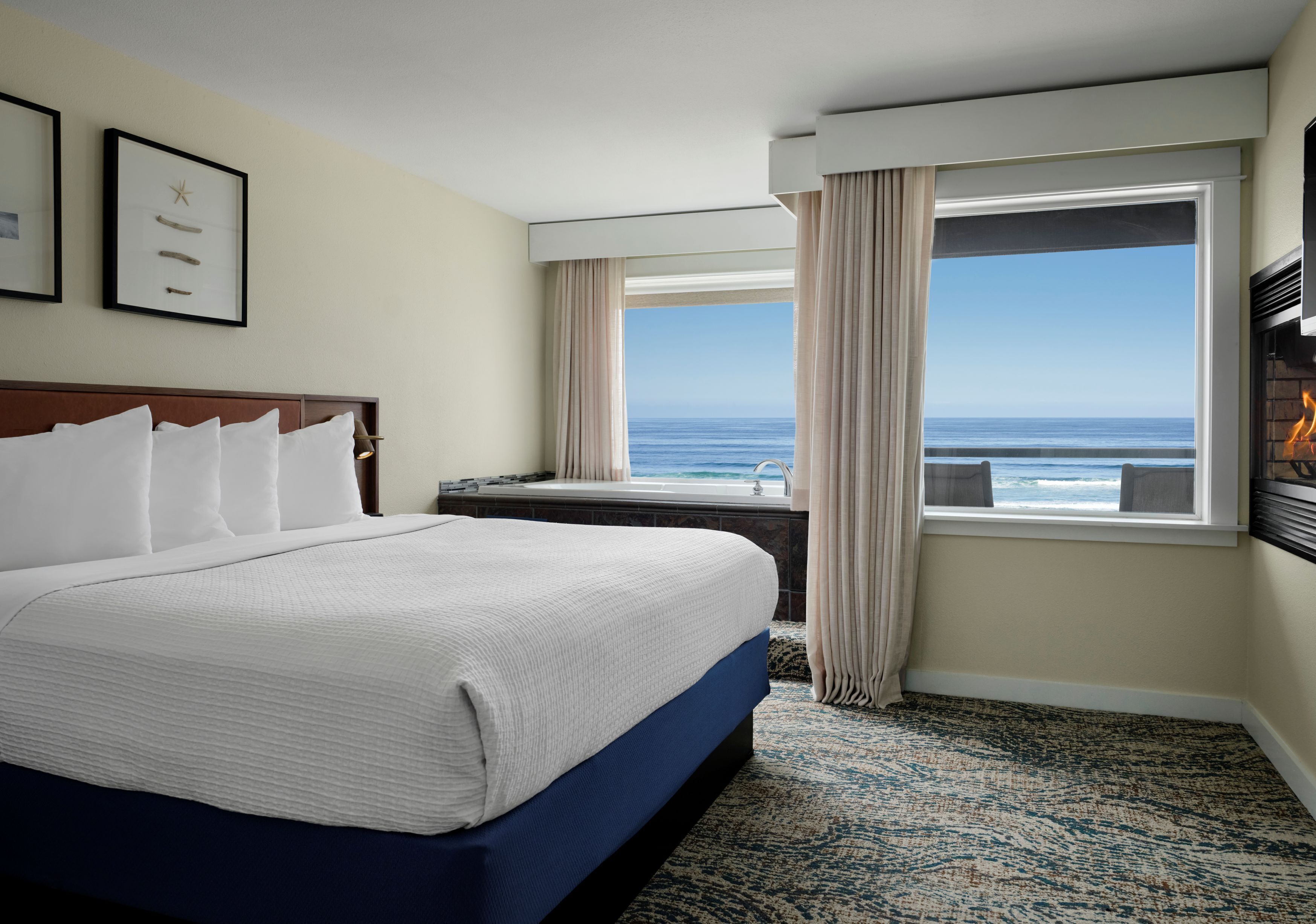 Una habitación de hotel con una cama grande, vista al océano, chimenea y cortinas.