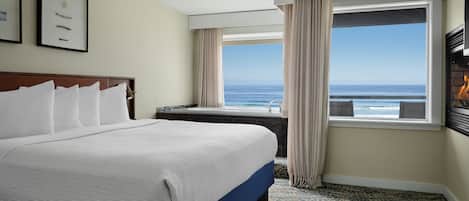 Une chambre d’hôtel avec un grand lit, une vue sur l’océan, une cheminée et une fenêtre avec des rideaux.