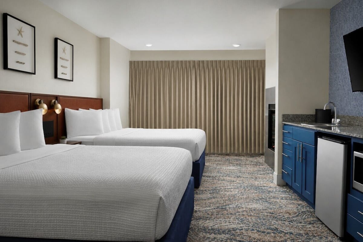 Ein Hotelzimmer mit zwei Betten, einem Schreibtisch, einem Fernseher und einem Badezimmer.