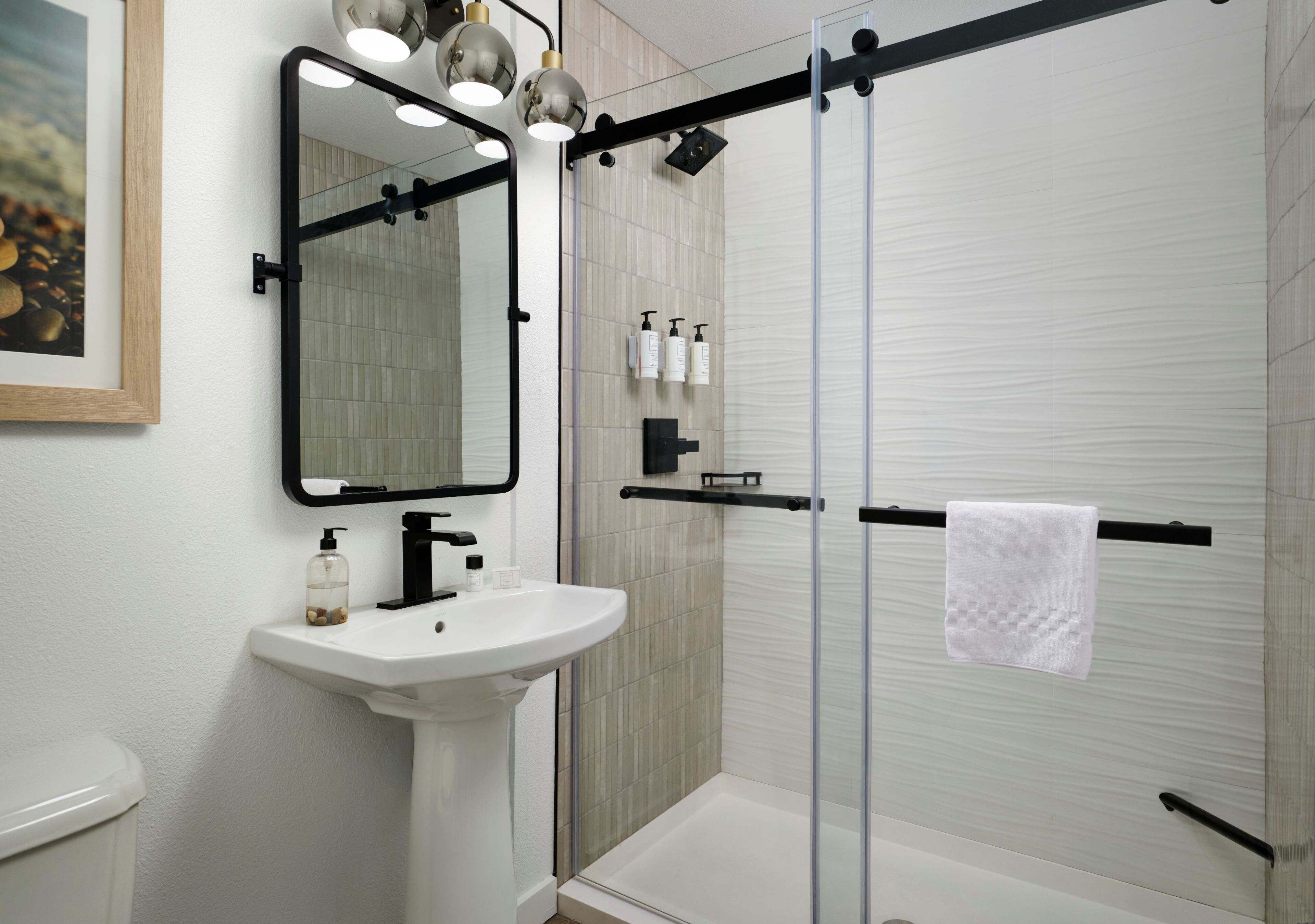 A bathroom with a white sink, a mirror, a glass shower enclosure, and a towel rack.