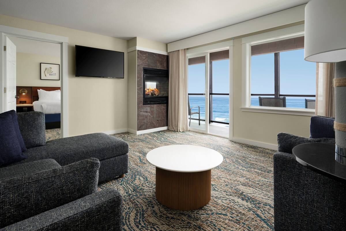 Ein Hotelzimmer mit großem Fenster, Flachbildfernseher, Kamin, rundem Couchtisch und einer Couch.