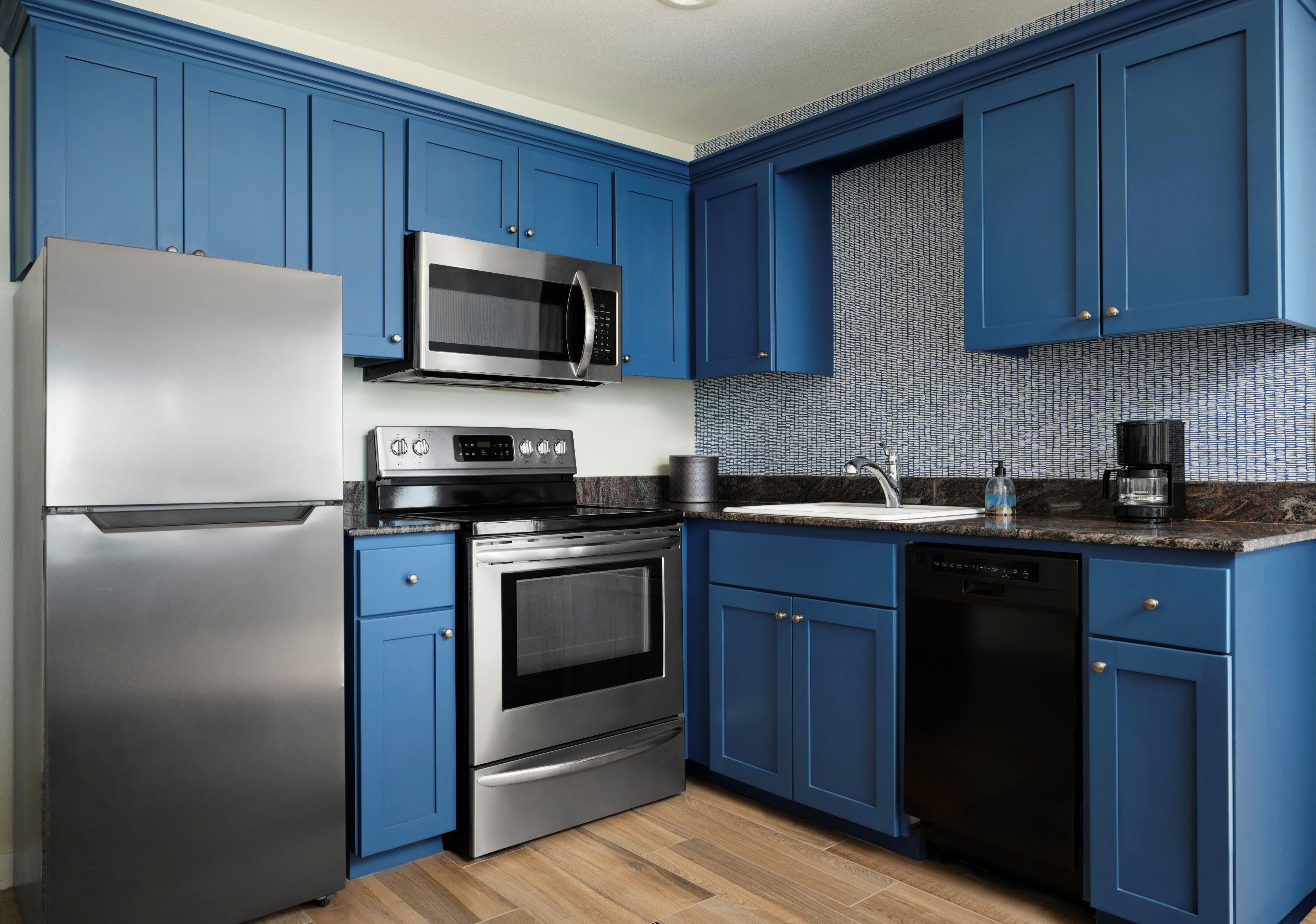 A kitchen with blue cabinets, stainless steel appliances, and a patterned backsplash.