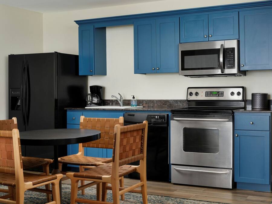 A kitchen with blue cabinets, a black refrigerator, a microwave, an oven, a dishwasher, and a round table with chairs.