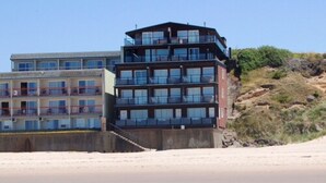 A multi-story hotel with balconies, a beach view, and a hilly backdrop. - Beachfront Manor Hotel (Lincoln City)