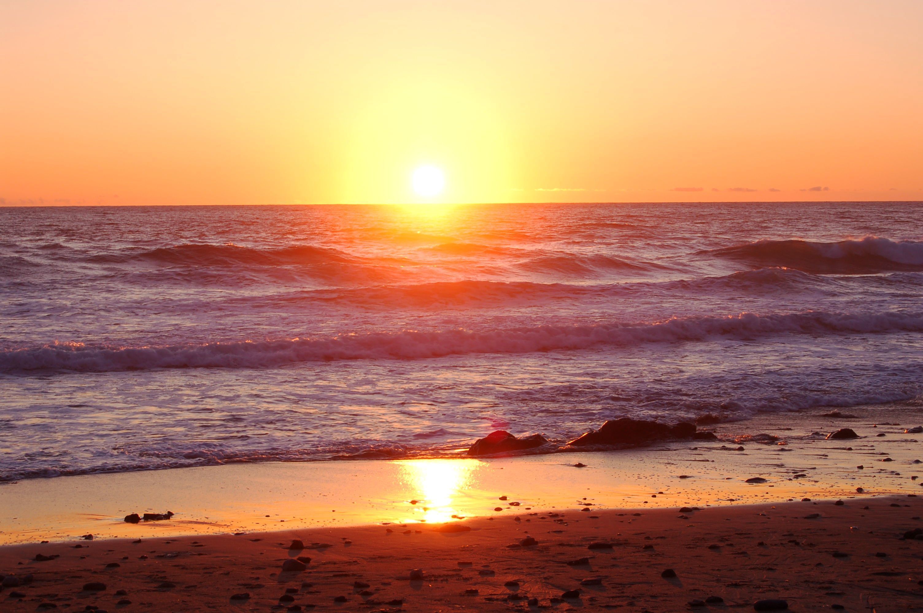 A beach at sunset with waves and a clear sky.