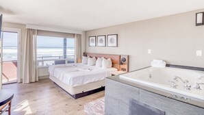 A hotel room with a large bed, a bathroom with a bathtub, and a view of the ocean. - Beachfront Manor Hotel (Lincoln City)