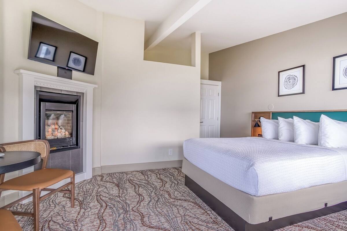 A hotel room with a bed, a fireplace, a dining table, and two framed pictures on the wall.