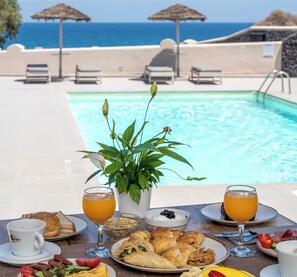 A table with breakfast items, a pool, and a view of the ocean. - En Plo Boutique Suites (Santorini)