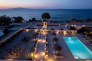 A rooftop pool area with lounge chairs, a swimming pool, and a view of the sea at dusk. - En Plo Boutique Suites (Santorini)