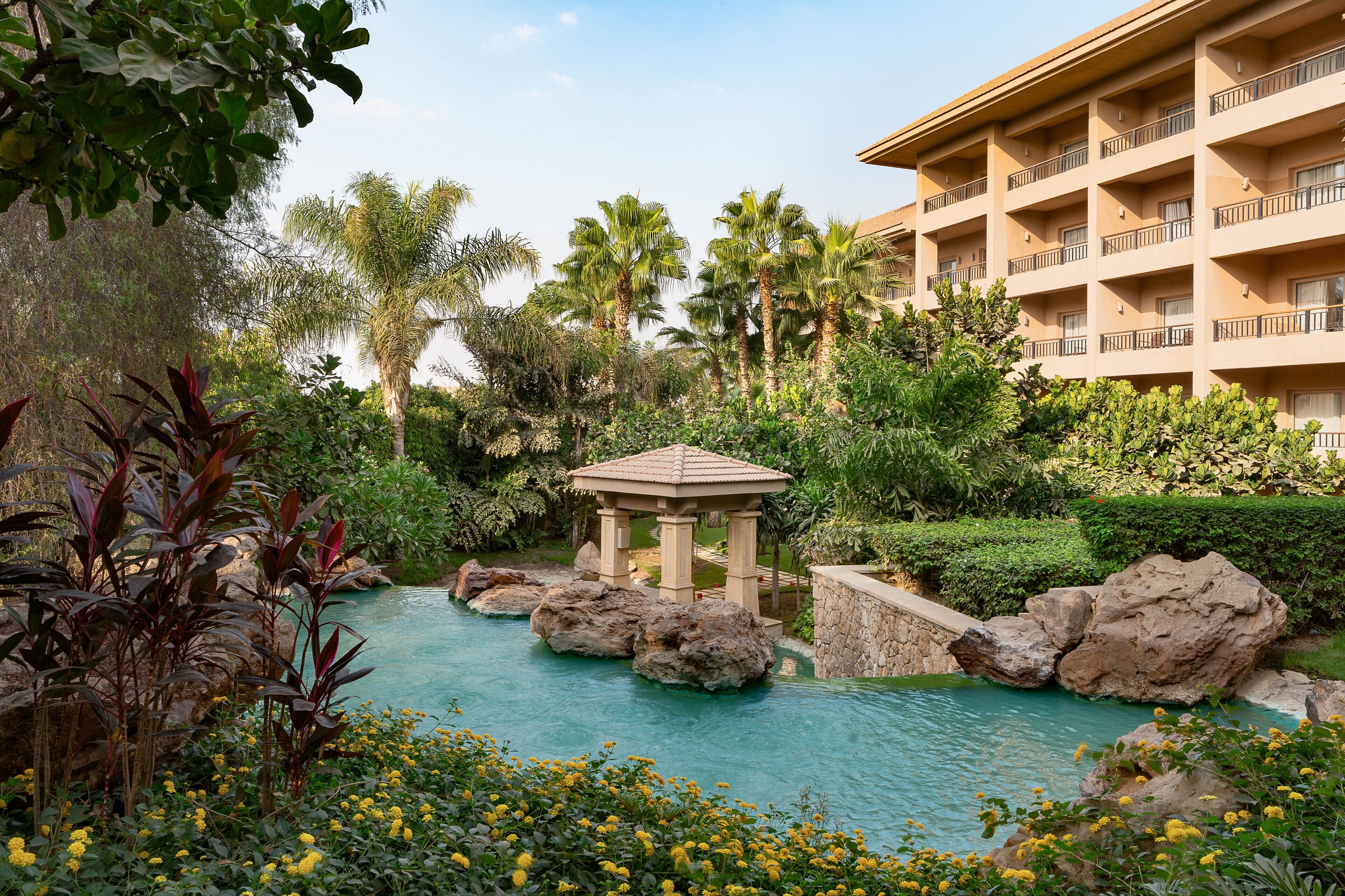 A hotel with a pool surrounded by tropical plants and palm trees.