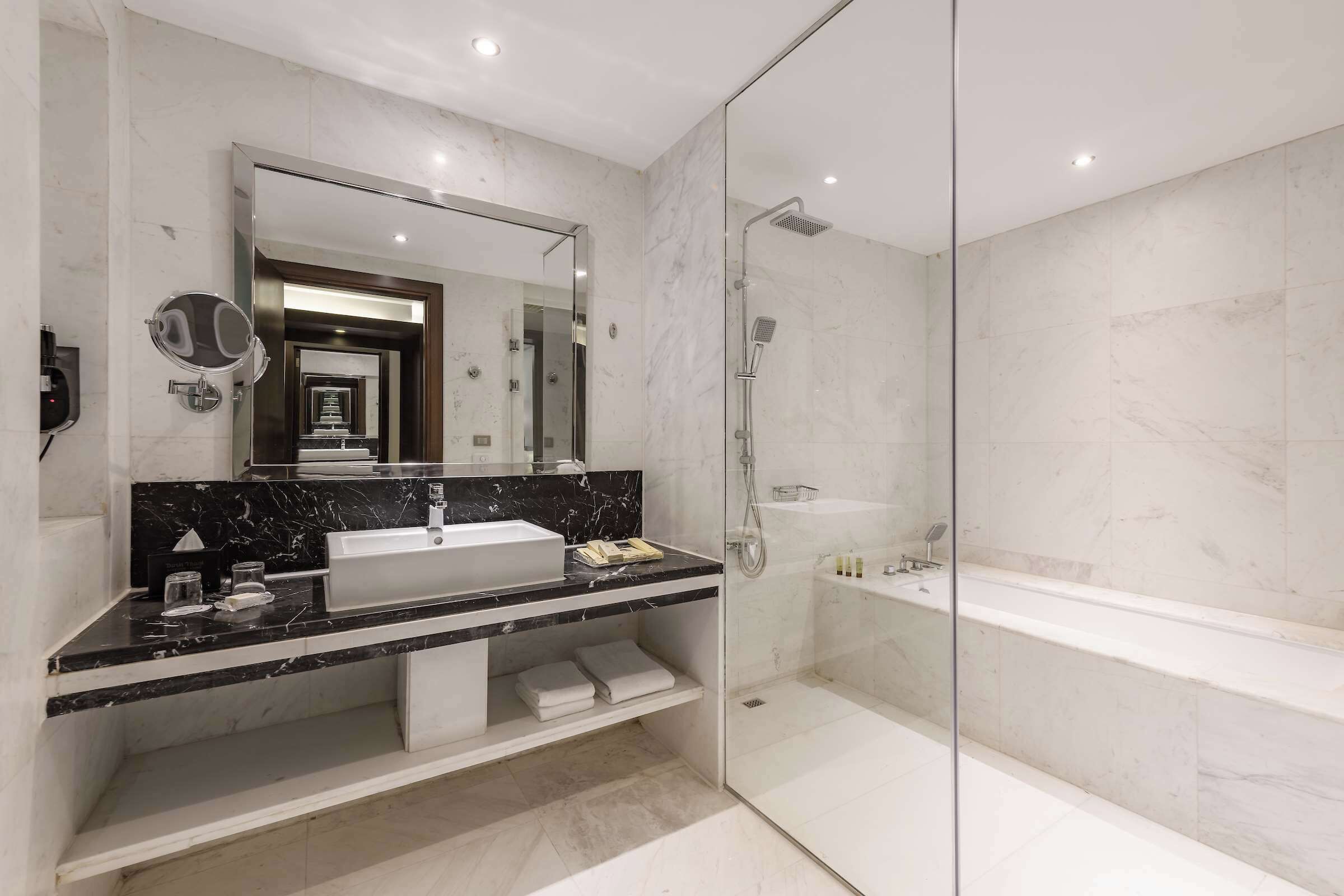 A modern bathroom with a glass-enclosed shower, a large mirror, and a marble countertop.